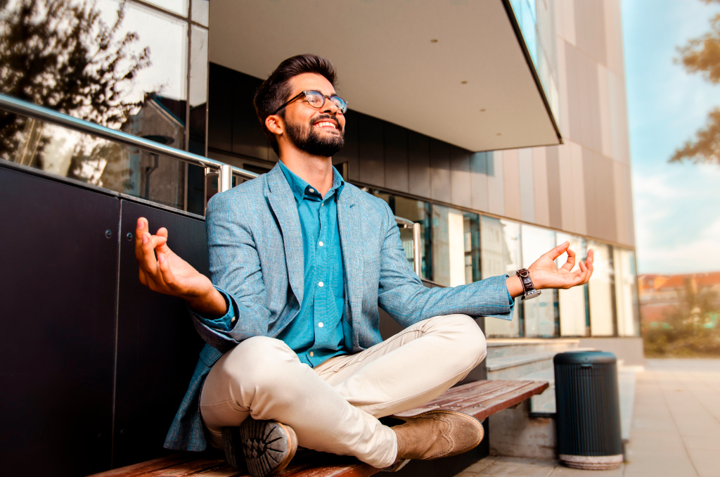 Businessman - mentally preparing for business meeting. Sitting in meditation pose in front of office building and smiling